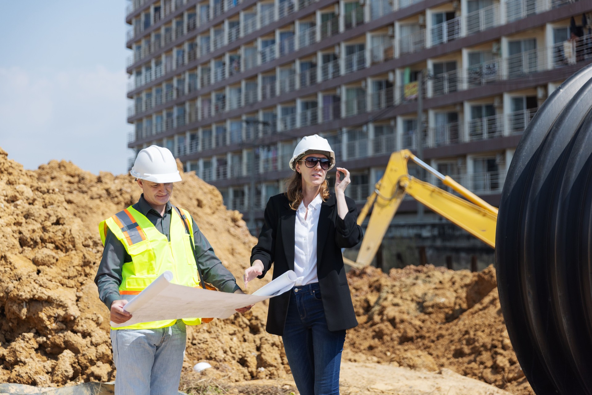 Two construction professionals discuss architectural blueprints at a building site